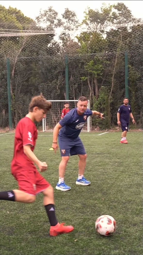 Un chico controla la pelota mientras el profe lo guía