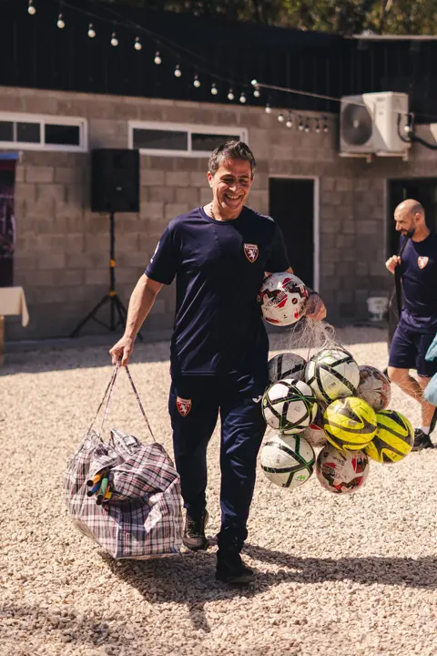 Entrenador de la academia llevando las pelotas a la cancha